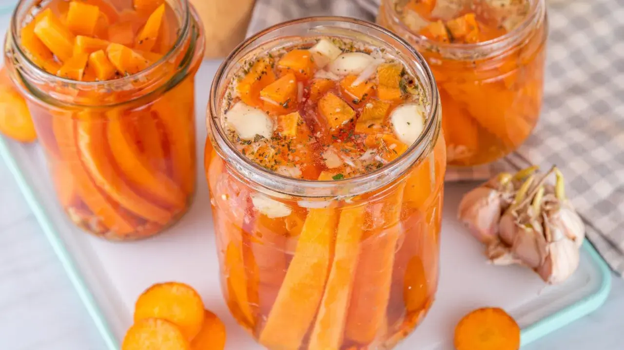 Gläser mit karotten fermentieren, gefüllt mit Karottenstücken, Knoblauch und Kräutern. Ein ganzer Knoblauch liegt daneben.