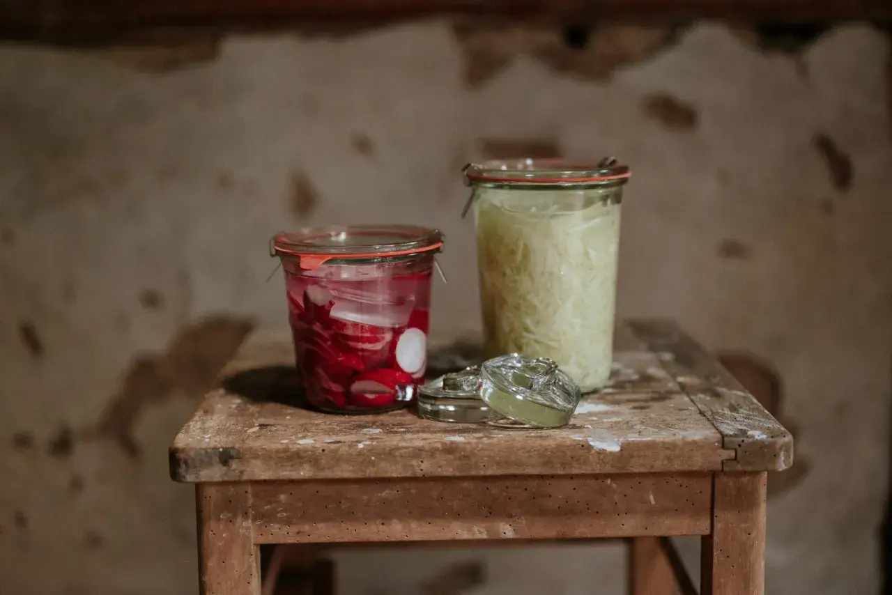 Zwei Gläser mit fermentierten Lebensmitteln: links eingelegte Radieschen, rechts fermentiertes Sauerkraut.