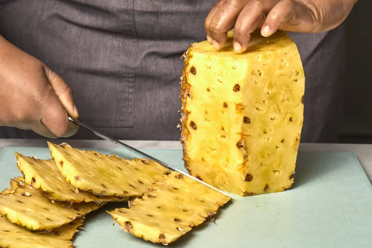 Hände schneiden eine Ananas. Dunkle Flecken auf der Frucht könnten ein Hinweis sein, um Ananas Schimmel zu erkennen.