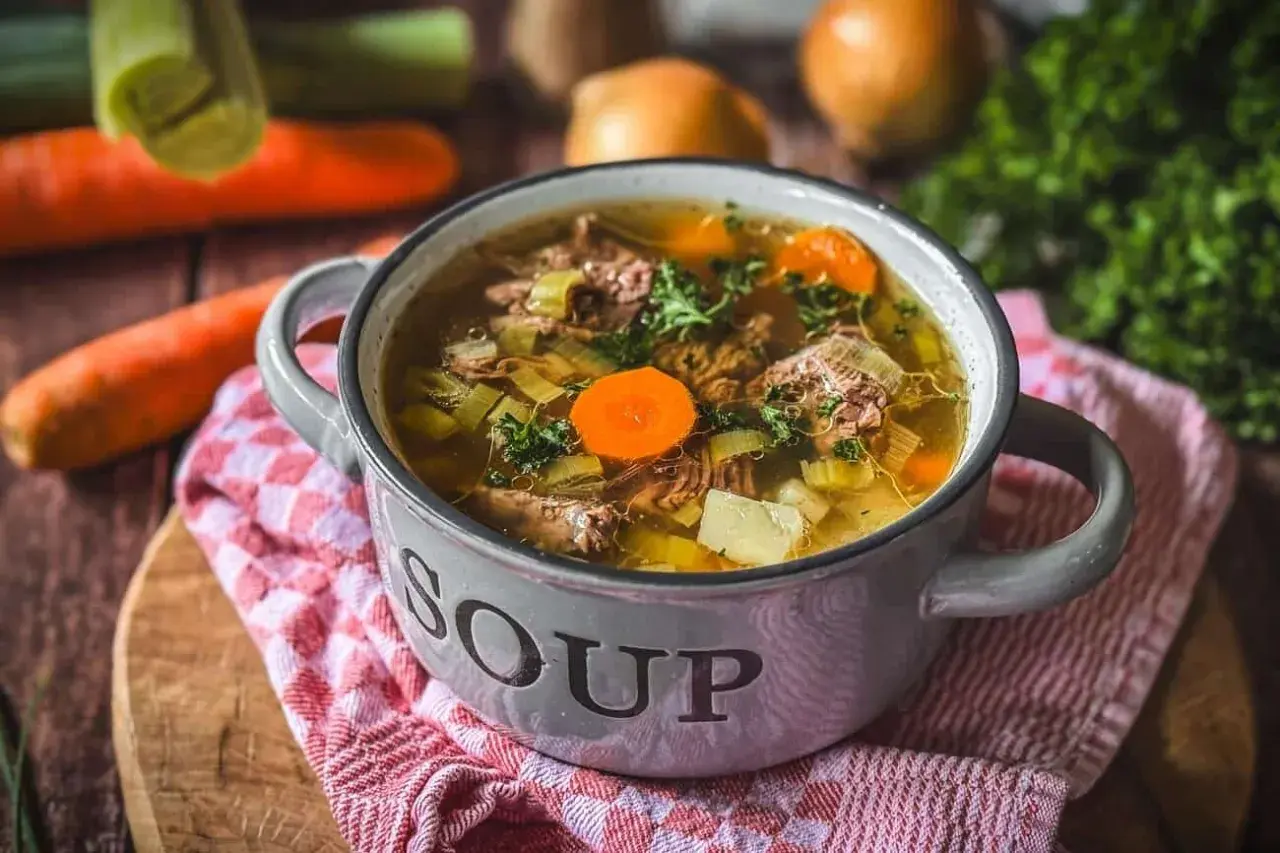 Eine dampfende Schüssel mit Omas frischer Suppe, gefüllt mit zartem Fleisch, Karotten, Sellerie und Kartoffeln.