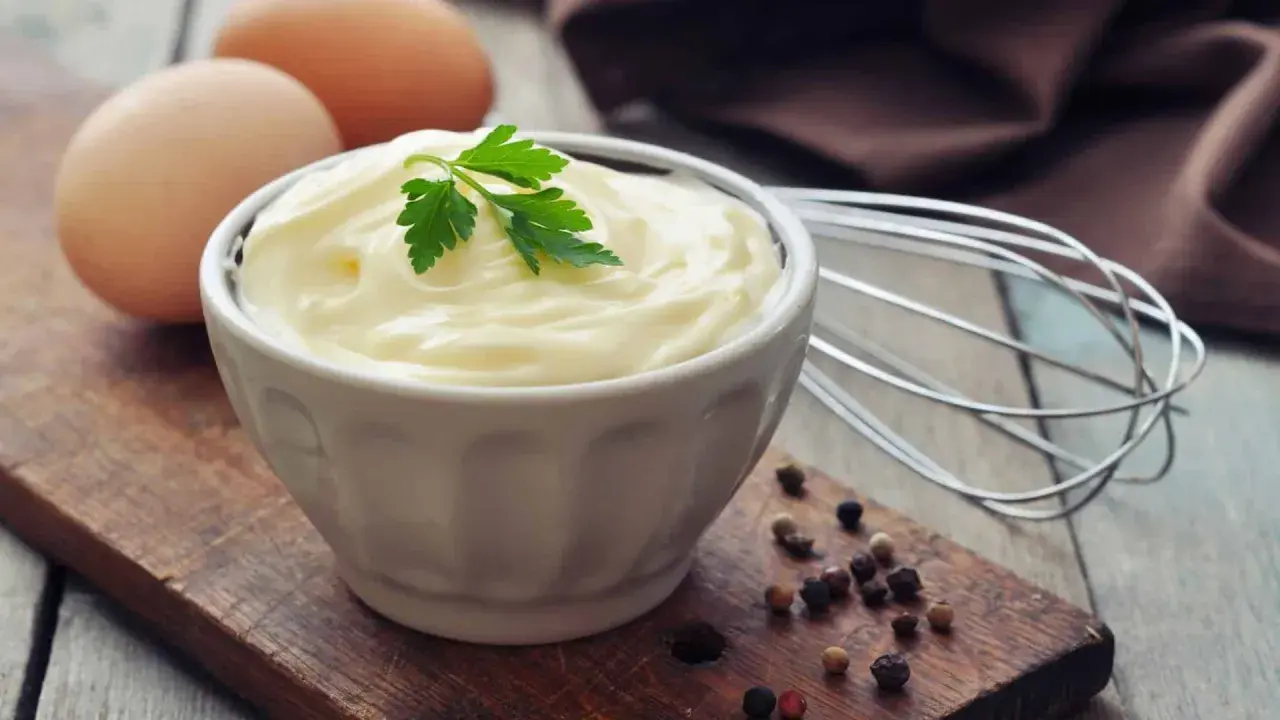 Frische Eier und Petersilie auf einem Holzbrett, bereit, um köstliche Mayonnaise selber zu machen. Ein Schneebesen liegt daneben.