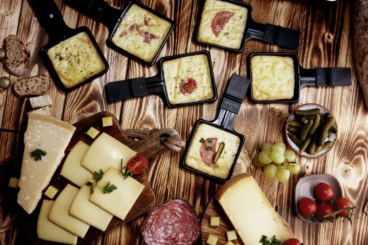 Raclette-Pfännchen mit geschmolzenem Käse, Brot, Käse, Salami, Cornichons und Trauben. Perfekt für einen gemütlichen Abend mit einem Glas Wein.