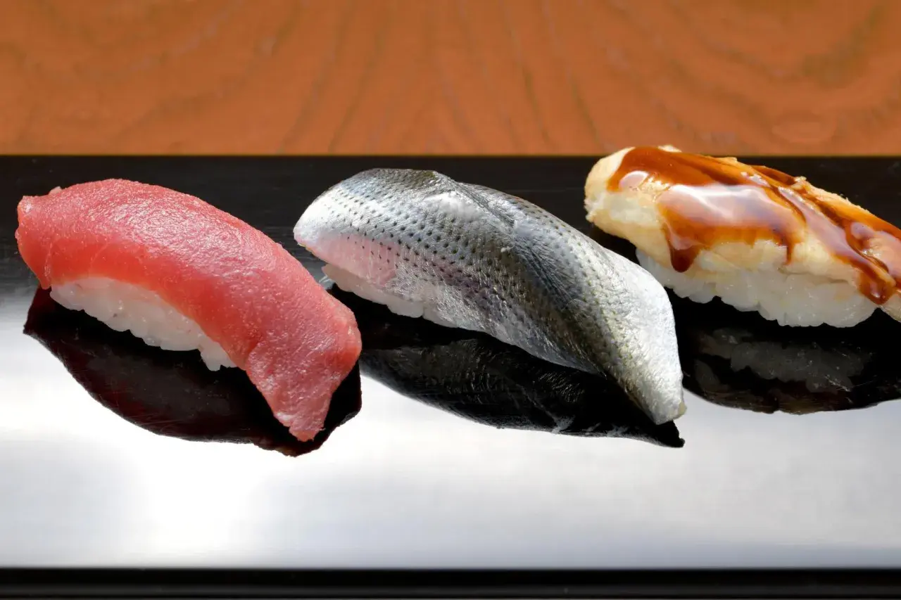 Drei exquisite Sushi-Rollen auf schwarzer Platte: roter Thunfisch, silberner Fisch mit Schuppen und ein mit Soße überzogener Fisch. Das teuerste Sushi der Welt, ein kulinarischer Genuss.