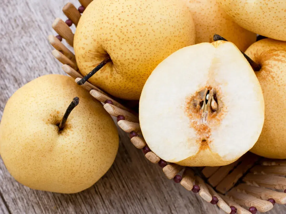 Nashi Birnen, deren Herkunft in Asien liegt, in einem Korb. Eine Frucht ist halbiert und zeigt das saftige Innere.