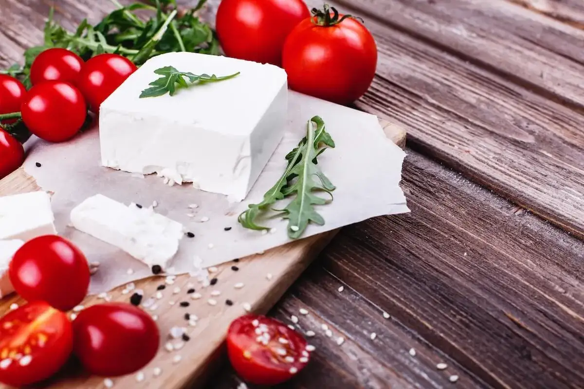 Frischer Feta, Tomaten und Rucola auf einem Holzbrett. Perfekt f&uuml;r alle, die Feta selber machen wollen.