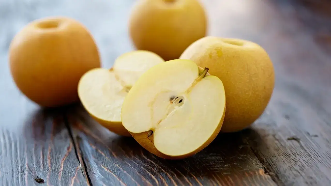So isst man eine Nashi Birne: Ganze Fr&uuml;chte und eine aufgeschnittene Nashi Birne liegen auf einem Holztisch.