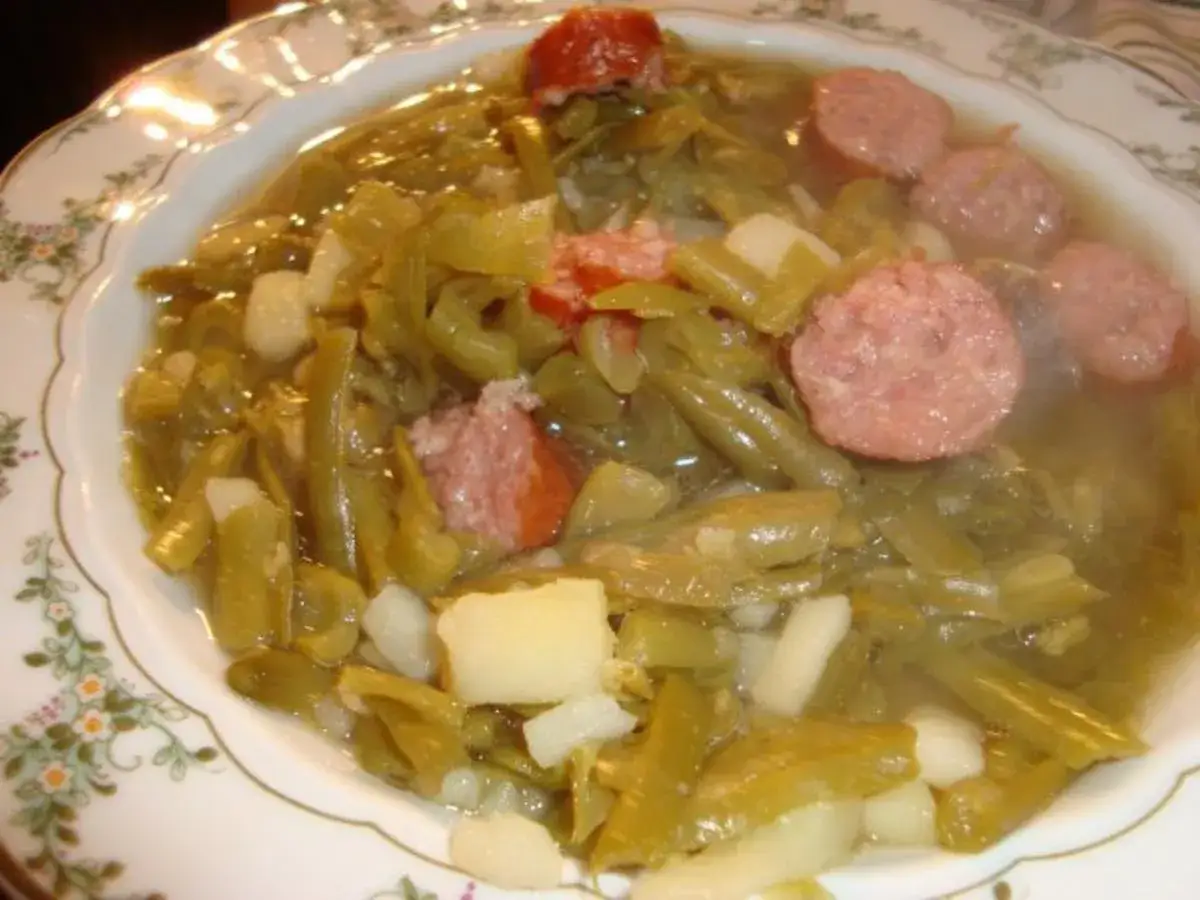 Ein Teller mit saure Bohnen Eintopf, Kartoffeln und Wurstscheiben.