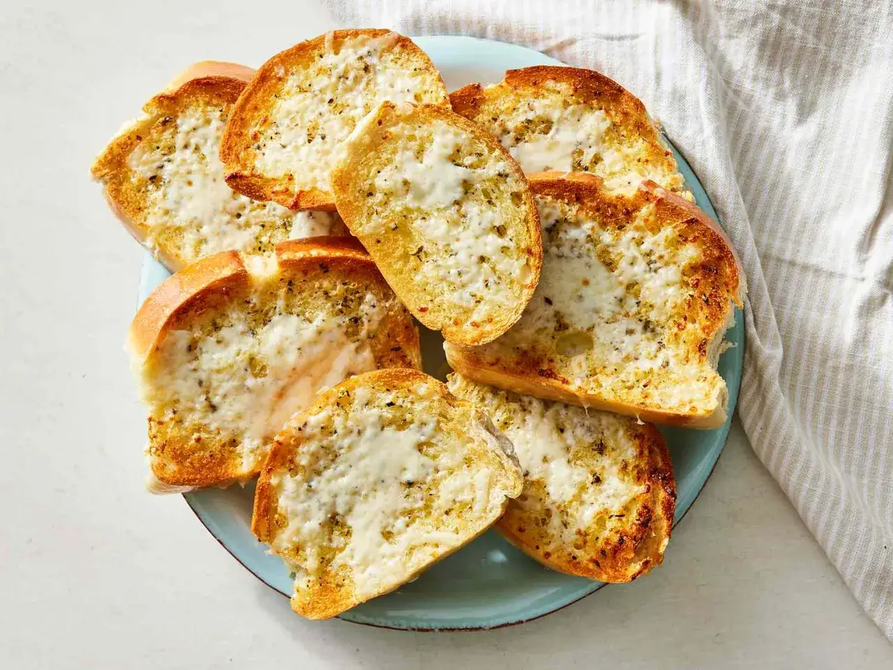 Knoblauchbrot selbst machen ist einfach! Goldbraune Scheiben Baguette mit geschmolzenem K&auml;se und Kr&auml;utern.