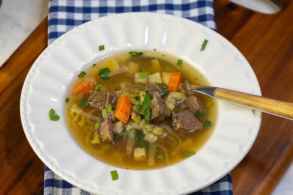 Eine dampfende Schüssel mit Omas frischer Suppe, gefüllt mit zarten Fleischstücken, Karotten, Kartoffeln und Kräutern.