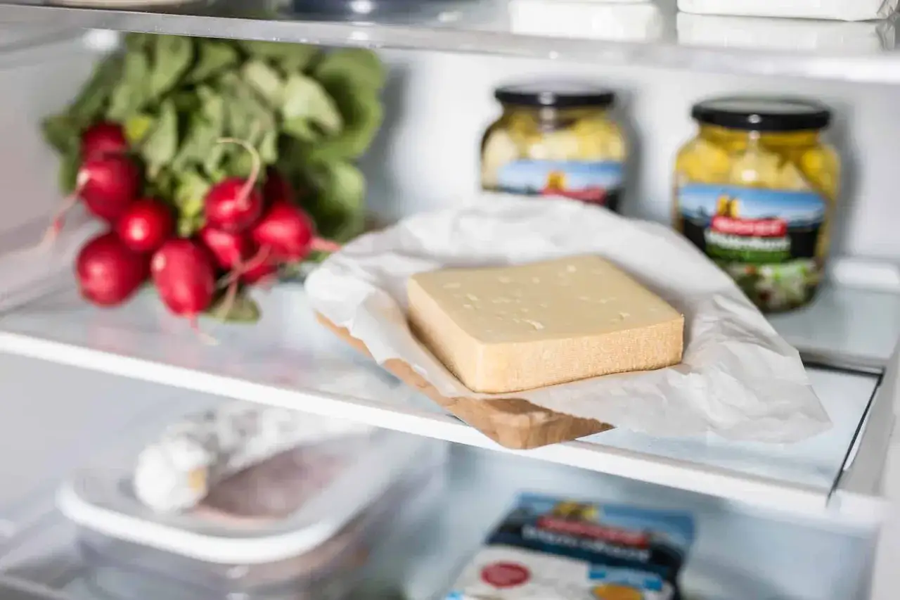 Ein Stück Käse liegt auf einem Holzbrettchen mit Papier im Kühlschrank. So lässt sich Käse, wie z.B. Feta, aufbewahren.