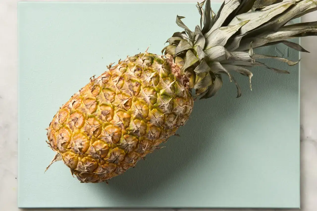Eine reife Ananas liegt auf einem mintgrünen Brett. Sie sieht so saftig aus, man könnte fast meinen, die Ananas schmeckt nach Alkohol.