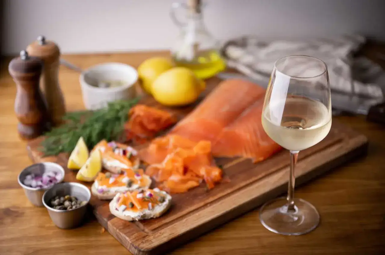 Ein Glas Weißwein neben Lachs, Zitronen und kleinen Broten mit Lachs. Die perfekte Antwort auf die Frage: welcher Wein zu Lachs.