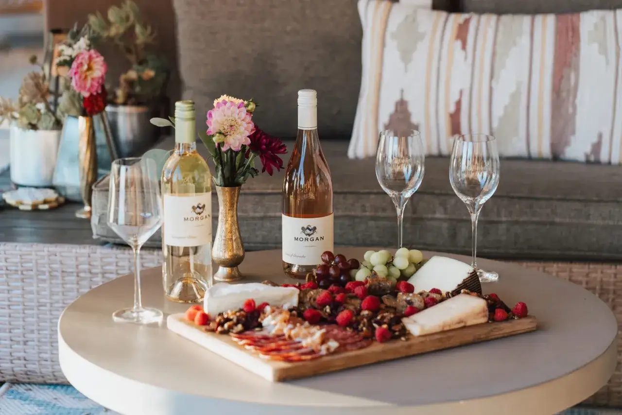 Ein Tisch mit Sauvignon Blanc, Käse, Früchten und Aufschnitt. Blumen in einer Vase schmücken die Szene.