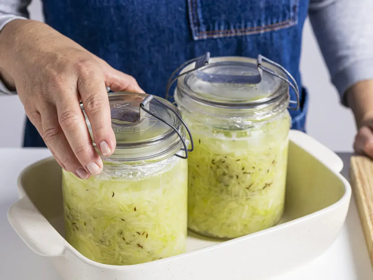 H&auml;nde platzieren zwei Gl&auml;ser mit fermentiertem Sauerkraut in einer Auflaufform.