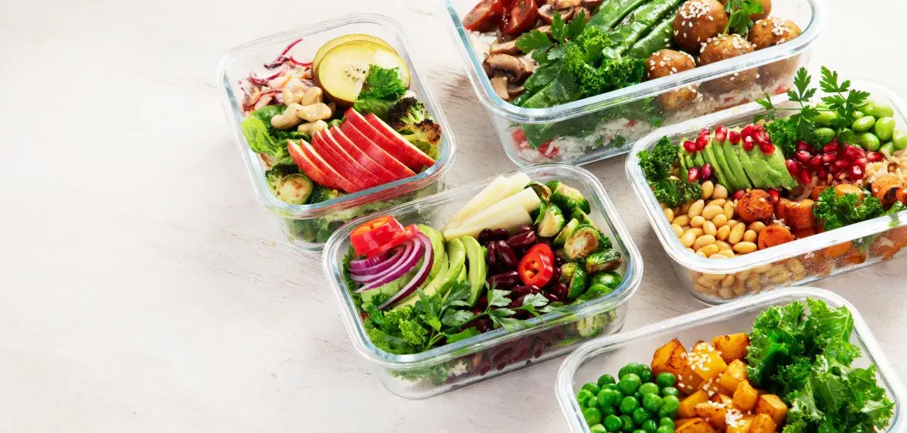 Mehrere Glasbeh&auml;lter mit bunten, gesunden gerichte zum vorkochen: Salate, Gem&uuml;se, Bohnen und Obst.