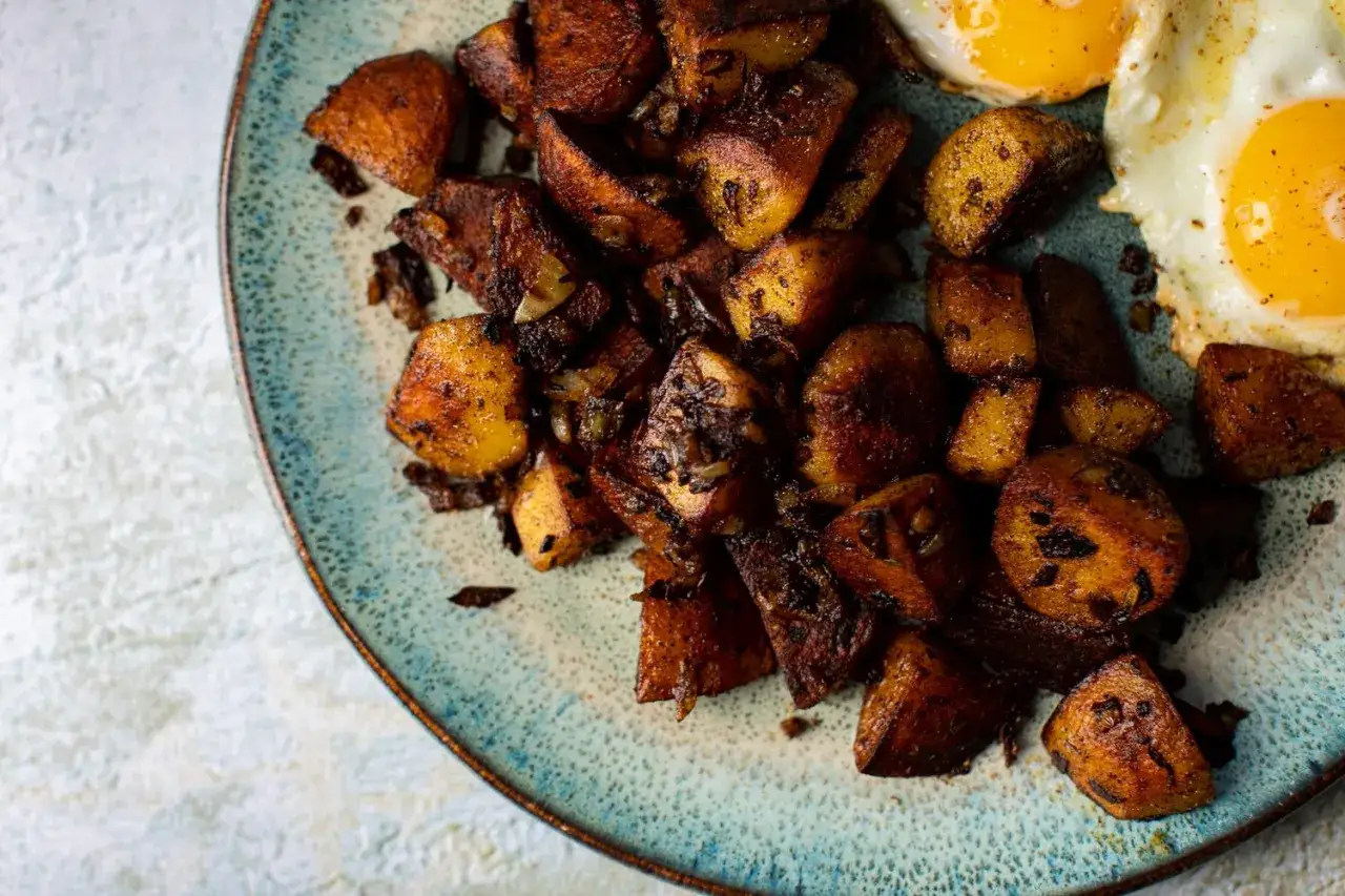 Knusprige Bratkartoffeln aus rohen Kartoffeln, goldbraun gebraten, mit zwei Spiegeleiern auf einem blauen Teller.