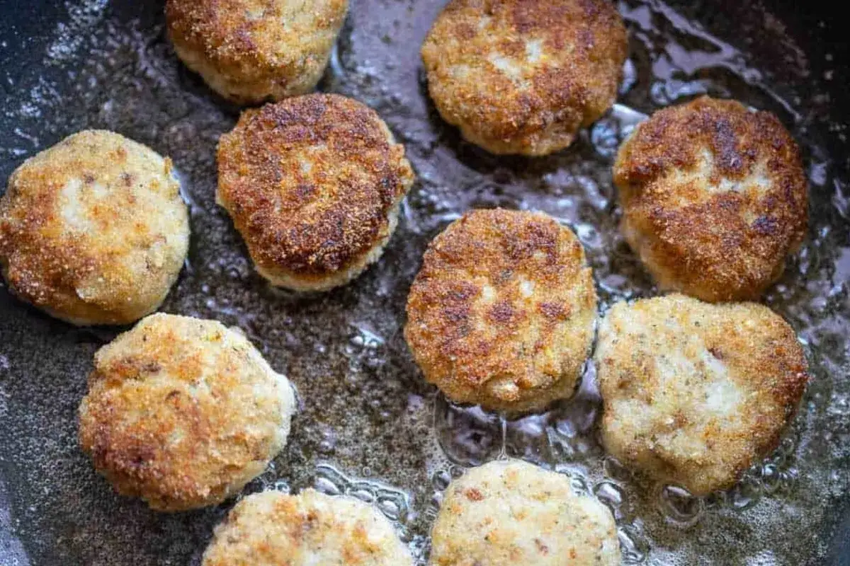 Mehrere goldbraune hackfleisch frikadellen brutzeln in heißem Öl in einer Pfanne.