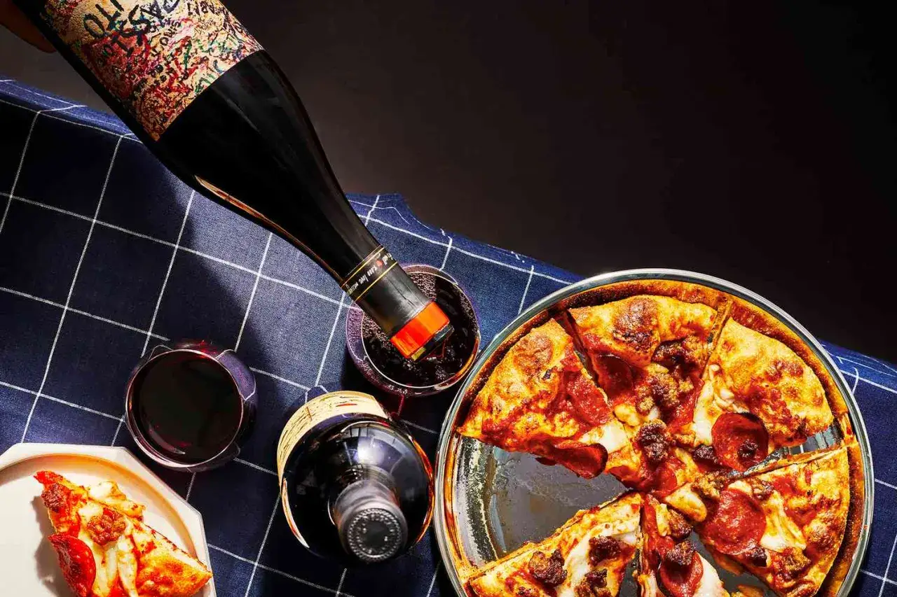 Ein Glas Rotwein wird in ein Glas gegossen, neben einer k&ouml;stlichen Pizza. Die perfekte Antwort auf die Frage: welcher Wein zu Pizza.