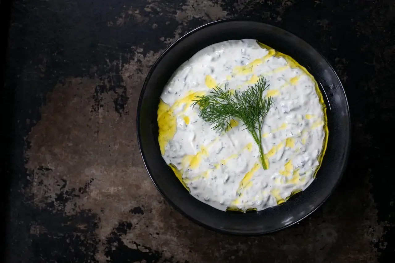 Cremiger griechischer Tzatziki, verfeinert mit Oliven&ouml;l und garniert mit frischem Dill, serviert in einer schwarzen Schale auf rustikalem Untergrund.