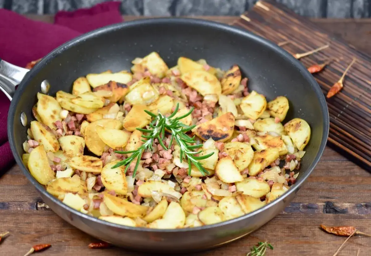 Bratkartoffeln mit gekochten Kartoffeln und Zwiebeln, garniert mit Rosmarin, in einer Pfanne.