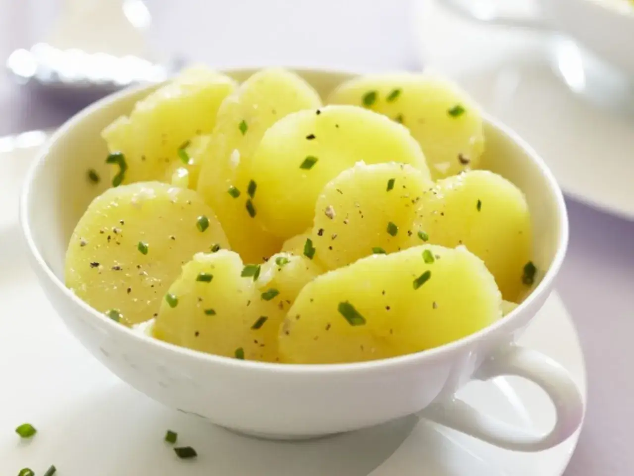 Ein Schälchen Kartoffelsalat für 4 Personen, garniert mit frischen Kräutern und Pfeffer.