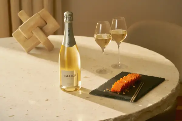 LALLIER Blanc de Blancs Champagner mit zwei Gläsern und einem Holzpuzzle.